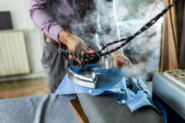 Genç erkek Afrikalı Amerikalı terzi atölyesinde ütü yapıyor..