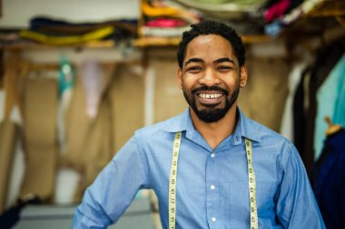 Genç Afrikalı Amerikalı terzi kendi atölyesinde gülümsüyor..