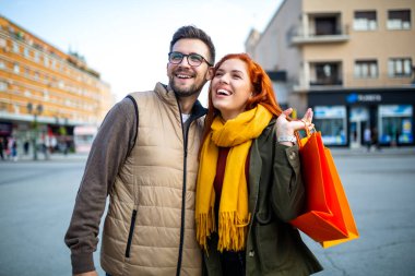 Güler yüzlü çift, alışveriş torbalarıyla şehir caddesini gezmekten ve yürümekten zevk alıyor.