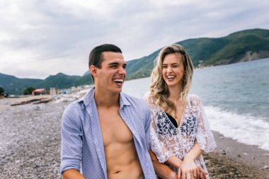 Mutlu genç çift sahilde gülüyor ve sarılıyor.