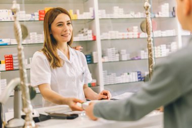 Kadın, eczacı reçeteli ilaç ya da eczanedeki ilaç için müşteriye danışmanlık yapıyor. Erkek doktor, sağlık hizmetleri için eczanede hastaya antibiyotik veriyor.