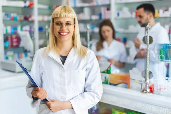 Smiling Portrait Young Beautiful Female Pharmacist Standing Clipboard Other Pharmacists — Stock Photo, Image
