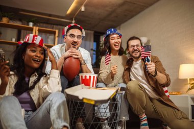 Amerikan bayraklarıyla ragbi izleyen çok ırklı bir arkadaş grubu..