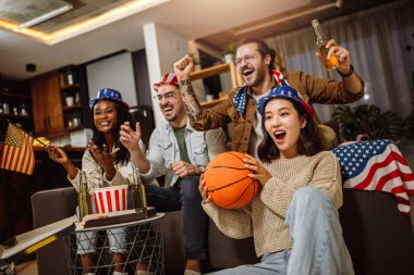 Amerikan bayraklarıyla basketbol maçı izleyen, bira içen ve tezahürat yapan çok ırklı arkadaş grubu..