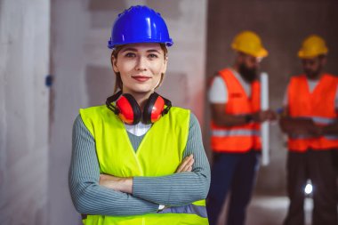 Sarı kask takan ve sarı yelek giyen başarılı kadın müteahhit portresi. İnşaat alanında durup kameraya bakan mimarın portresi..