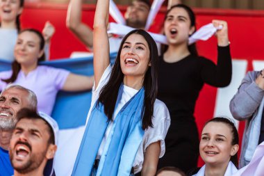 Spor taraftarları stadyumdaki maçta tezahürat yapıyor. Takımlarını desteklemek için mavi ve beyaz renkler giyiyorlar. Bayrak ve eşarplarla kutlama.