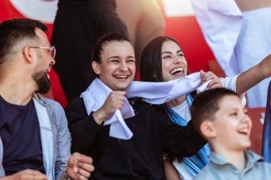 Spor taraftarları stadyumdaki maçta tezahürat yapıyor. Takımlarını desteklemek için mavi ve beyaz renkler giyiyorlar. Bayrak ve eşarplarla kutlama.