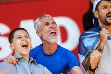 Spor taraftarları stadyumdaki maçta tezahürat yapıyor. Takımlarını desteklemek için mavi ve beyaz renkler giyiyorlar. Bayrak ve eşarplarla kutlama.