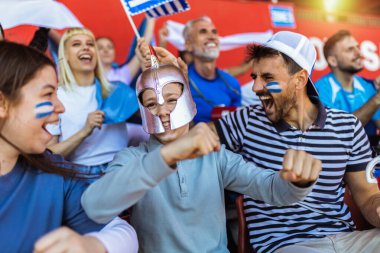 Yunanistan taraftarları stadyumdaki maçta tezahürat yapıyorlar. Takımlarını desteklemek için mavi ve beyaz renkler giyiyorlar. Bayrak ve eşarplarla kutlama.