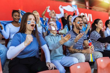 Yunanistan taraftarları stadyumdaki maçta tezahürat yapıyorlar. Takımlarını desteklemek için mavi ve beyaz renkler giyiyorlar. Bayrak ve eşarplarla kutlama.