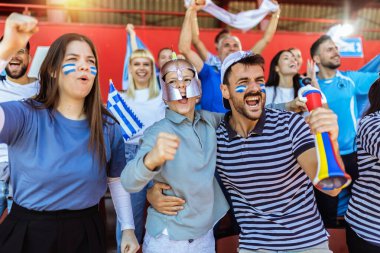 Yunanistan taraftarları stadyumdaki maçta tezahürat yapıyorlar. Takımlarını desteklemek için mavi ve beyaz renkler giyiyorlar. Bayrak ve eşarplarla kutlama.