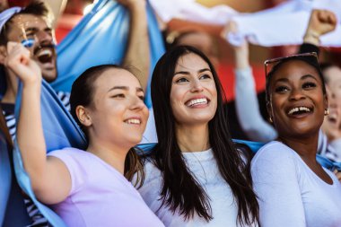 Spor taraftarları stadyumdaki maçta tezahürat yapıyor. Takımlarını desteklemek için mavi ve beyaz renkler giyiyorlar. Bayrak ve eşarplarla kutlama.