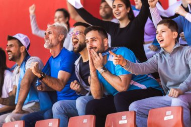 Spor taraftarları stadyumdaki maçta tezahürat yapıyor. Takımlarını desteklemek için mavi ve beyaz renkler giyiyorlar. Bayrak ve eşarplarla kutlama.