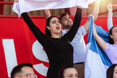 Spor taraftarları stadyumdaki maçta tezahürat yapıyor. Takımlarını desteklemek için mavi ve beyaz renkler giyiyorlar. Bayrak ve eşarplarla kutlama.