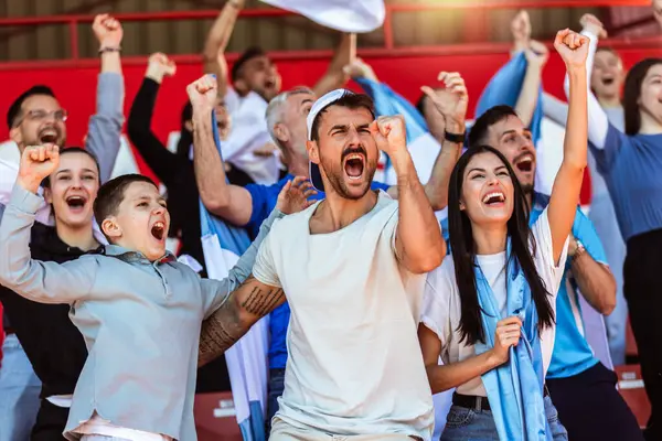 Spor taraftarları stadyumdaki maçta tezahürat yapıyor. Takımlarını desteklemek için mavi ve beyaz renkler giyiyorlar. Bayrak ve eşarplarla kutlama.