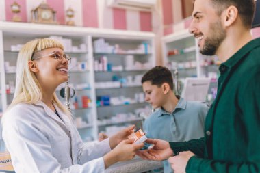 Neşeli genç sarışın eczacı kadın vitamin ve ilaç veriyor baba ve oğluna.
