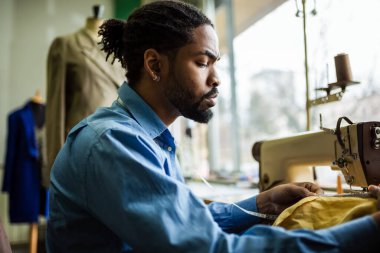 Afro-Amerikalı erkek moda tasarımcısı, atölyesindeki kumaşı ölçen terzi..