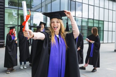 Arkadaşlarının önünde toga ve diplomayla duran yüksek lisans öğrencisinin portresi..