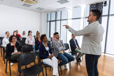 Erkek CEO, çok ırklı bir grup meslektaşın önünde duruyor ve soruyu cevaplaması için birini çağırıyor. Akıllı tahtası olan çokluortam sınıfı.