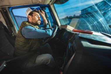 Yorgun bir kamyon şoförü mola verip kamyonunda dinleniyor.