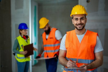 İnşaat müdürü çelik yelek ve kask giyip kağıda yazı yazıyor..