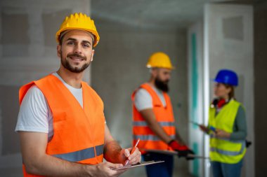 İnşaat müdürü çelik yelek ve kask giyip kağıda yazı yazıyor..