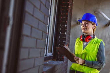 Sarı kask takan ve sarı yelek giyen başarılı kadın müteahhit portresi. İnşaat alanında duran ve kağıda bir şeyler yazan mimarın portresi. İşlerin nasıl gittiğini araştırıyor..