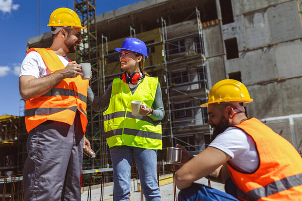 Три строителя пьют кофе и обедают на стройке.