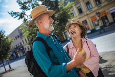 Yeni şehri keşfeden yaşlı evli bir çift. Şapka ve sırt çantası takıyorlar..