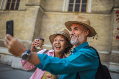 Yaşlı evli bir çift kahve molasındayken selfie çekiyor. Yeni şehri keşfeden turistler.