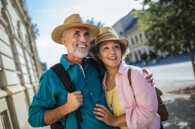 Yeni şehri keşfeden yaşlı evli bir çift. Şapka ve sırt çantası takıyorlar..