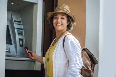 Kadın Afro-Amerikalı turist ATM makinesinin başında pimini çekmeye hazırlanıyor..