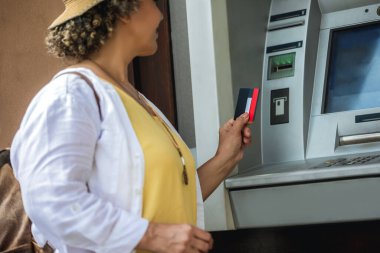 Kadın Afro-Amerikalı turist ATM makinesinin başında pimini çekmeye hazırlanıyor..