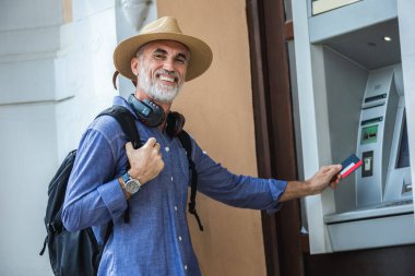 ATM makinesinin önünde kredi kartıyla duran yaşlı turist..