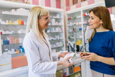 Neşeli eczacı kadın modern eczanedeki genç bayana vitamin ve antibiyotik veriyor..