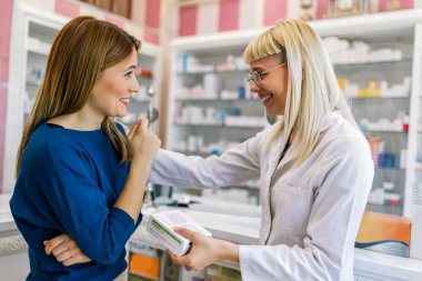 Neşeli eczacı kadın modern eczanedeki genç bayana vitamin ve antibiyotik veriyor..