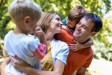 Parkta dört kişilik bir aile. Anne ve baba oğullarıyla kucaklaşıyor..