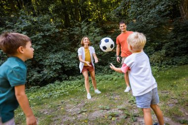 Dört kişilik aile parkta futbol oynuyor..