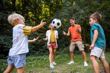 Dört kişilik aile parkta futbol oynuyor..