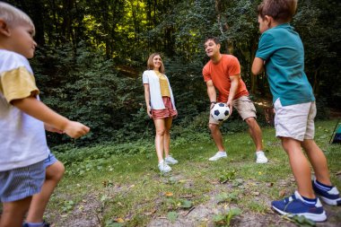 Dört kişilik aile parkta futbol oynuyor..