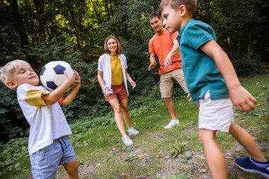 Dört kişilik aile parkta futbol oynuyor..