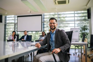 Meslektaşlarının önünde oturan genç iş adamının portresi..