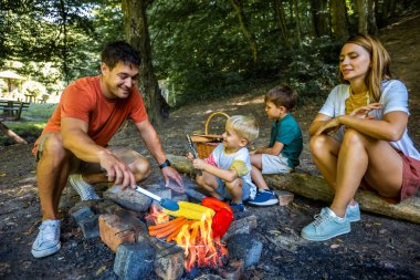 Baba oğul sebze ve et pişiriyorlar. Dört kişilik aile ormanda öğle yemeği molası veriyor..
