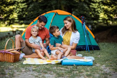 Ebeveynler kamp yaparken çocuklarıyla kucaklaşıyorlar. Çadır kuruldu ve aile güzel günün tadını çıkarıyor..