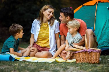 Dört kişilik mutlu bir aile çadırlarının önünde kamp yaparken iyi vakit geçiriyor..