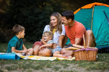 Aileler kamp yaparken parktaki çadırın önünde oğullarına sarılıyorlar..