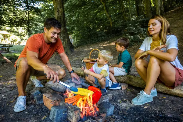 Baba oğul sebze ve et pişiriyorlar. Dört kişilik aile ormanda öğle yemeği molası veriyor..