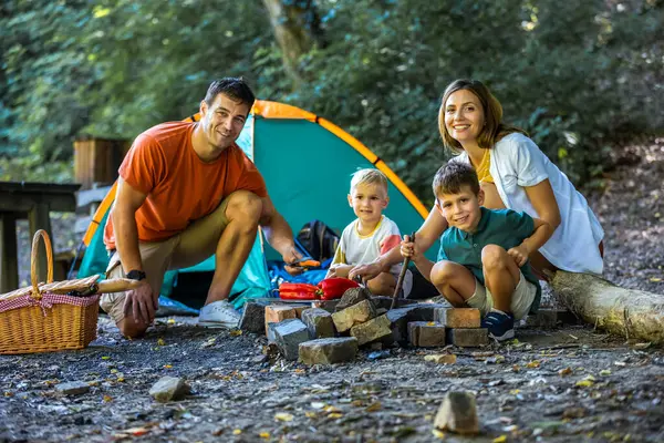Ormandaki çadırlarının önünde ızgaranın başında oturan dört kişilik bir aile portresi. Doğayı keşfetmenin uzun gününden sonra.