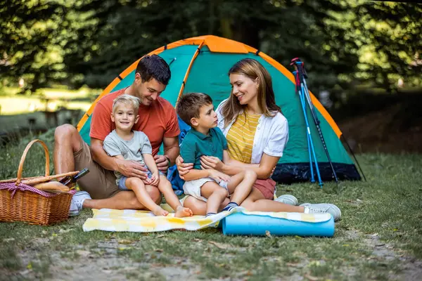 Ebeveynler kamp yaparken çocuklarıyla kucaklaşıyorlar. Çadır kuruldu ve aile güzel günün tadını çıkarıyor..