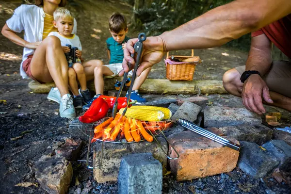Sebze ve et ızgarası yapan bir adamın yakın çekimi. Ormanda kamp yapan dört kişilik bir aile. Kampta öğle yemeği molası.